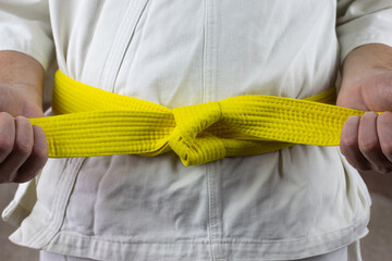Male hands tighten yellow belt in Kyokushin karate, Asian types of martial arts with belts, the...