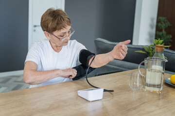 Senior caucasian woman measures her blood pressure at home using a tonometer. Everyday health checkup