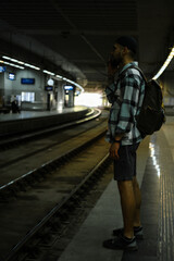 A young man travels alone with a backpack. The guy is standing on the platform, talking on the phone and waiting for his train. Side view. A railway station in Belgrade, Serbia.