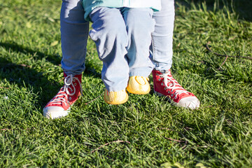 A person in jeans standing next to a child in red sneakers