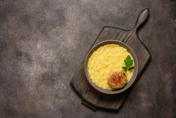 Mashed potatoes with meat cutlet in a bowl on a wooden board, dark grunge background. Top view, flat lay, copy space.