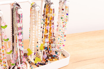 Different handcraft chains of beads, pearls and natural stones hanging on a stand with copy space.