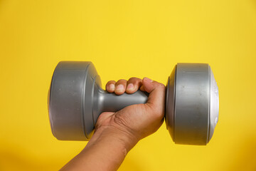 Male hand holding plastic dumbbell weighing three kilogram on a yellow background