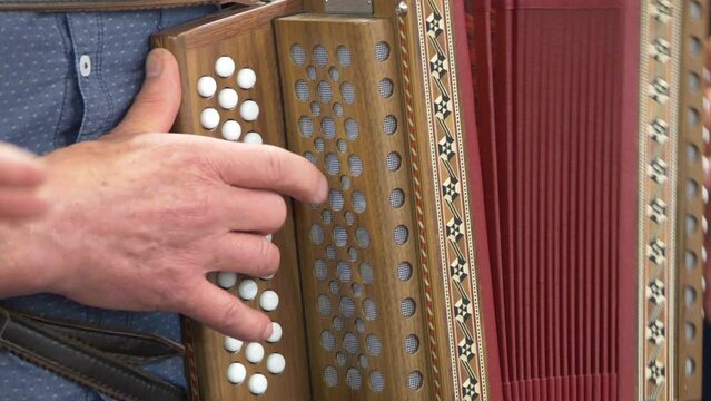 Closeup footage of the hands of a male musician playing on a diatonic-button accordion outdoor
