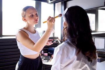 A charming blonde makeup artist applies makeup to her attractive client