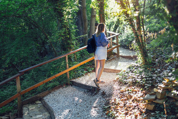 Young woman in shorts and shirt climbs steps of small pebbles and wooden boards on forest path.