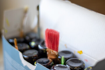 A box filled with colorful jars of paint and various sizes of brushes