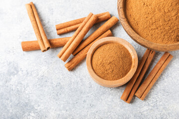 Cinnamon powder in a bowl on a textured wooden background. Spicy spice for baking, desserts and drinks. Fragrant ground cinnamon. Cinnamon stick. Place for text. Copy space.