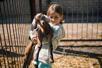 portrait of a child with a little goat in her arms on a farm