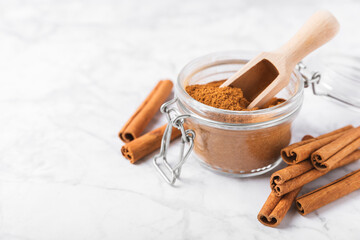 Cinnamon powder in a bowl on a textured wooden background. Spicy spice for baking, desserts and drinks. Fragrant ground cinnamon. Cinnamon stick. Place for text. Copy space.