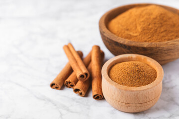 Cinnamon powder in a bowl on a textured wooden background. Spicy spice for baking, desserts and drinks. Fragrant ground cinnamon. Cinnamon stick. Place for text. Copy space.