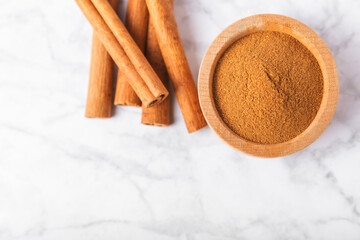 Cinnamon powder in a bowl on a textured wooden background. Spicy spice for baking, desserts and drinks. Fragrant ground cinnamon. Cinnamon stick. Place for text. Copy space.