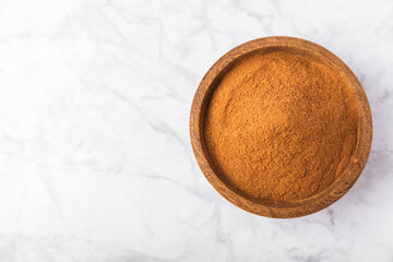 Cinnamon powder in a bowl on a textured wooden background. Spicy spice for baking, desserts and drinks. Fragrant ground cinnamon. Cinnamon stick. Place for text. Copy space.