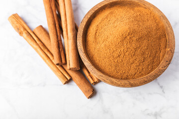 Cinnamon powder in a bowl on a textured wooden background. Spicy spice for baking, desserts and drinks. Fragrant ground cinnamon. Cinnamon stick. Place for text. Copy space.