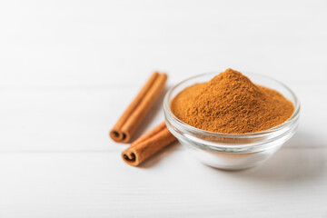 Cinnamon powder in a bowl on a textured wooden background. Spicy spice for baking, desserts and drinks. Fragrant ground cinnamon. Cinnamon stick. Place for text. Copy space.