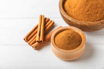 Cinnamon powder in a bowl on a textured wooden background. Spicy spice for baking, desserts and drinks. Fragrant ground cinnamon. Cinnamon stick. Place for text. Copy space.