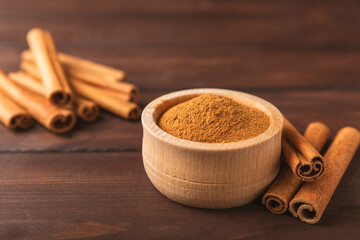 Cinnamon powder in a bowl on a textured wooden background. Spicy spice for baking, desserts and drinks. Fragrant ground cinnamon. Cinnamon stick. Place for text. Copy space.