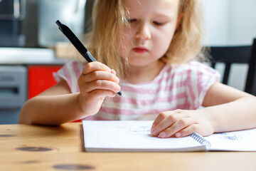 portrait of a girl sitting at the table in the kitchen and drawing in a notebook.