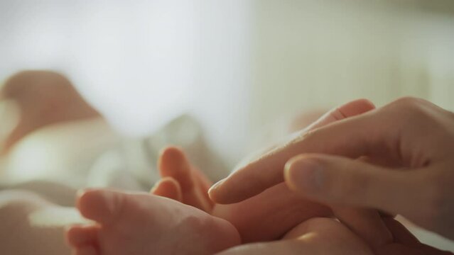 A happy mother gently strokes her baby's little feet, expressing her endless love and care. Moments of motherhood and manifestations of love in every touch of your child