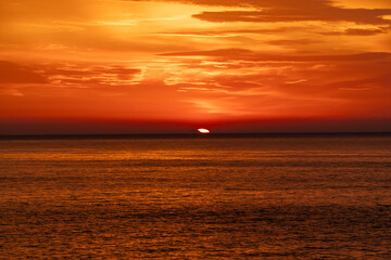 Obraz premium A beautiful coastal area in eastern part of Japan. A clear blue sky and an orange sunrise reflects on the sea water. A big rock formation in the coast line. Island from the distance.