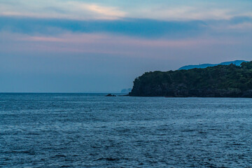 A beautiful coastal area in eastern part of Japan. A clear blue sky and an orange sunrise reflects on the sea water. A big rock formation in the coast line. Island from the distance.