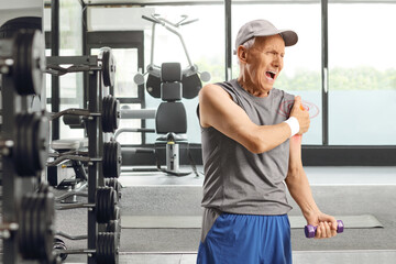 Elderly man in sportswear exercising at a gym and holding his shoulder