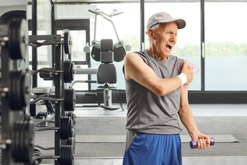Obraz premium Elderly man in sportswear exercising at a gym and holding his shoulder