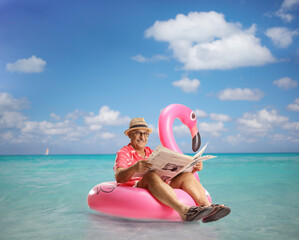 Mature man sitting on a flamingo swimming ring and reading a newspaper