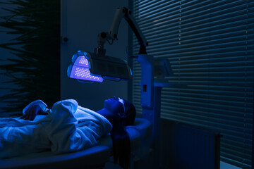 Remote view of female patient undergoes blue LED light therapy for skin rejuvenation at modern...