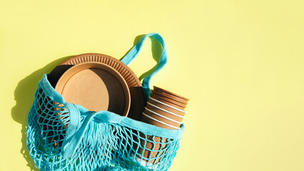 A set of paper utensils in mesh blue bag on a yellow background. Eco friendly, zero waste concept....