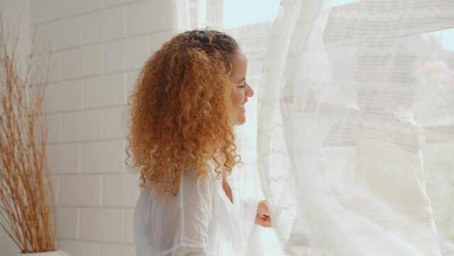 Cheerful mother playing with daughter hiding behind the curtains in living room at home. Little cute girl tease and enjoy with mother in bedroom at house. Family relationship concept.
