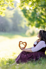 beautiful, young, bavarian woman in traditional costume, dirndl, sitting in nature on the meadow in...