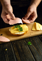 Preparing sandwiches for a snack on a vintage kitchen table. Male hands put sausage on cheese.
