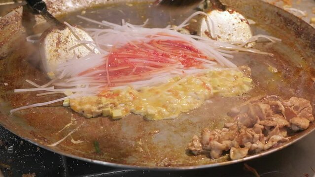 cooking pad thai on metal baking sheet, classic Thai dish from fried rice noodles, slow motion
