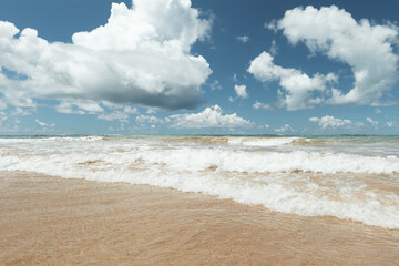 A tropical beach in Brazil with waves and a sky with lots of clouds.