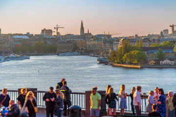 Stockholm, Södermalm, Sweden. Tourists and locals at the Fjällgatan street viewpoint, overlooking the old town, the Stockholm inlet and the Grand Hotel with Skeppsholmen on the right at sunset