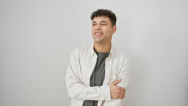 Cheerful young arab man in casual clothes striking a confident profile pose, looking to the side with a natural smile and relaxed attitude on isolated white wall.
