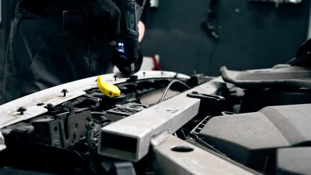 close-up At a service station master auto mechanic is tightening the bolts on the front panel of the car
