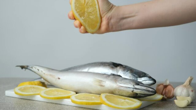 The process of squeezing lemon juice from half a lemon onto uncooked sea fish mackerel before cooking.
