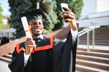 Happy African American student taking selfie with cell phone on their graduation day