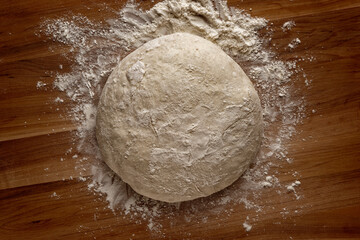 Top view of a ball of bread dough on a wooden board with flour