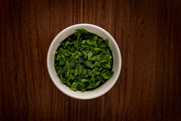 Top view of a bowl full of chopped basil on a wooden table