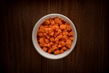 Small bowl of raw diced carrots on a wooden table