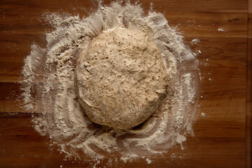 Top view of a ball of bread dough on a wooden board with flour