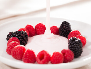 Fresh raspberries and blackberries laid out on a white plate in circle with yogurt