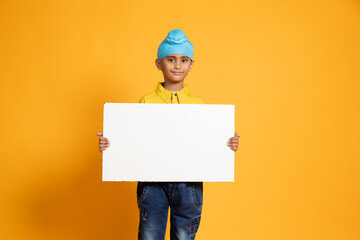 Happy Indian sikh boy kid holding place card isolated on yellow background. Education, Advertising,...