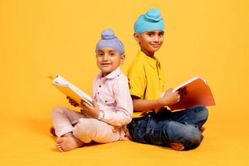 Portrait of Two smiling indian sikh school students sitting on floor holding note books studying...