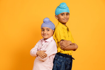 Portrait of two confident Indian sikh punjabi boy kids standing arms crossed isolated over yellow...