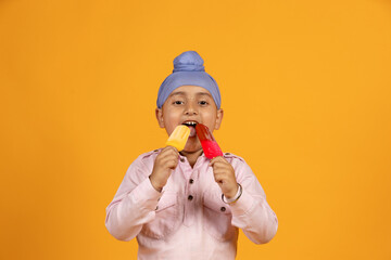 Portrait of Sikh Indian kid enjoy two different flavor ice cream or ice lolly in summer isolated...