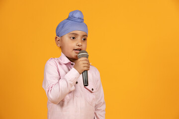 Cute Indian playful sikh boy kid singing song in mic isolated on orange background. Childhood...